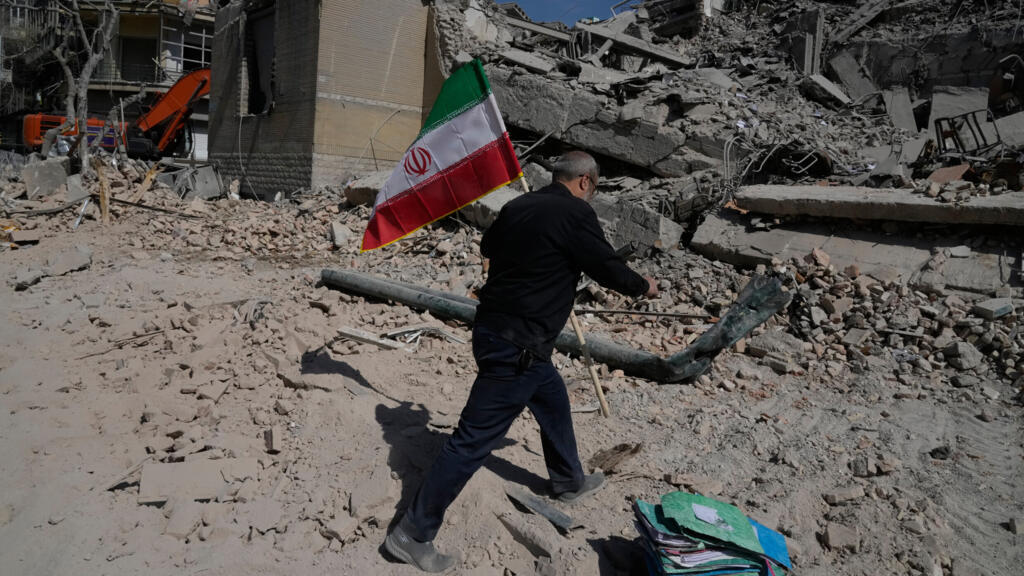 Un homme porte un drapeau de la République islamique d'Iran pour le placer sur les décombres d'un poste de police touché lors de la campagne militaire américano-israélienne à Téhéran, en Iran, le mercredi 4 mars 2026. Un homme porte un drapeau de la République islamique d'Iran pour le placer sur les décombres d'un poste de police touché lors de la campagne militaire américano-israélienne à Téhéran, en Iran, le mercredi 4 mars 2026.